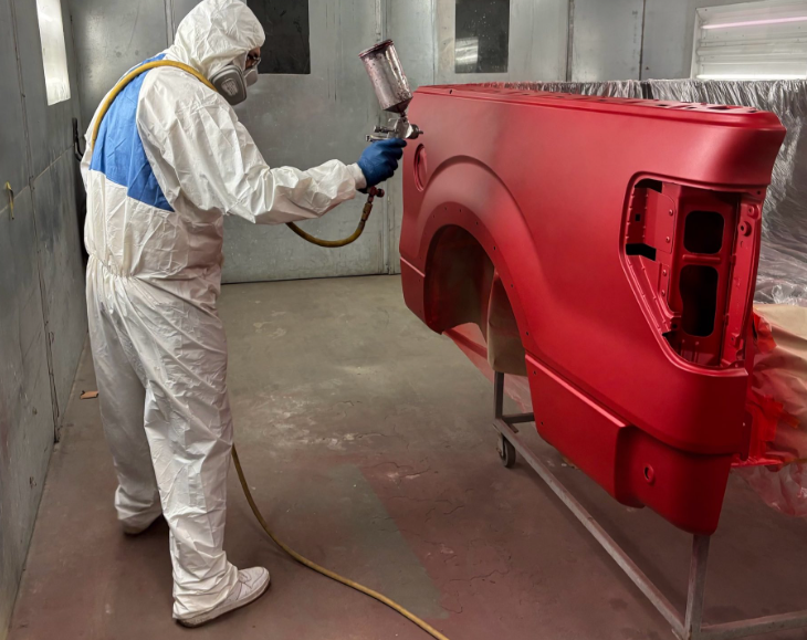Auto body technician painting a repaired car in a collision repair shop in Mishawaka, Indiana