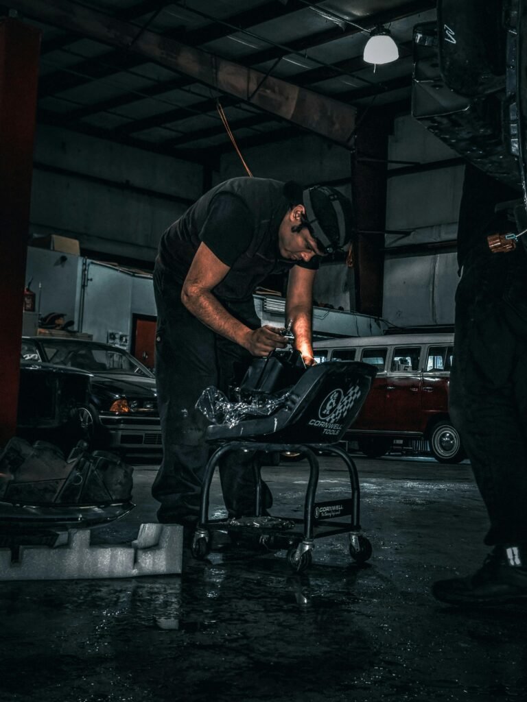 A mechanic focused on a car part repair in a dimly lit auto body shop.