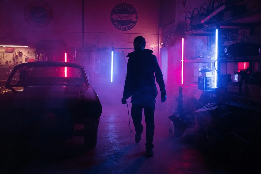 A mechanic in a neon-lit garage works amidst vibrant pink and blue lights, creating a moody, cyberpunk atmosphere.